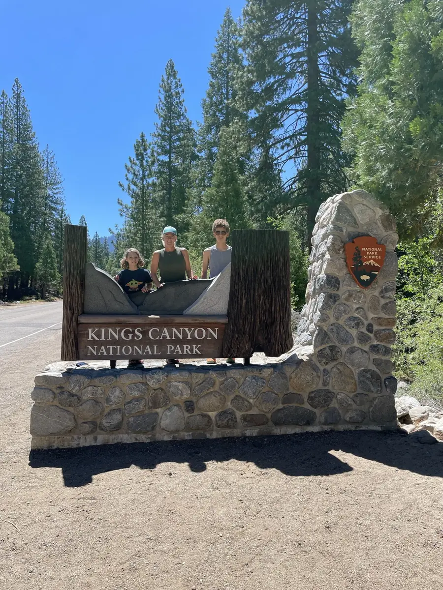 Three hikers at the Kings Canyon National Park entrance sign